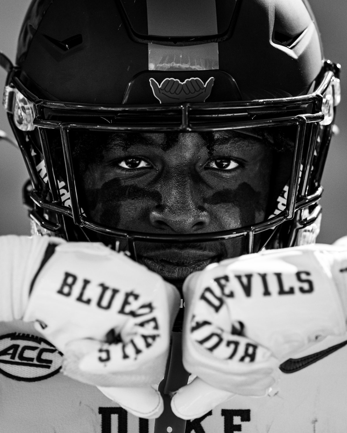 Duke Football player in a close-up black and white portrait, gloves reading Blue Devils